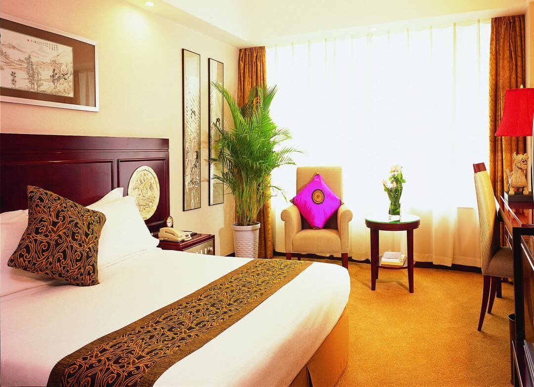 A hotel room with a large bed, a chair, a small table, and a potted plant.