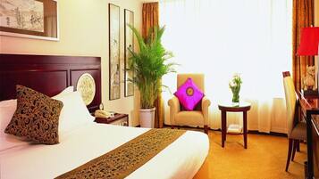 A hotel room with a large bed, a chair, a small table, and a potted plant.