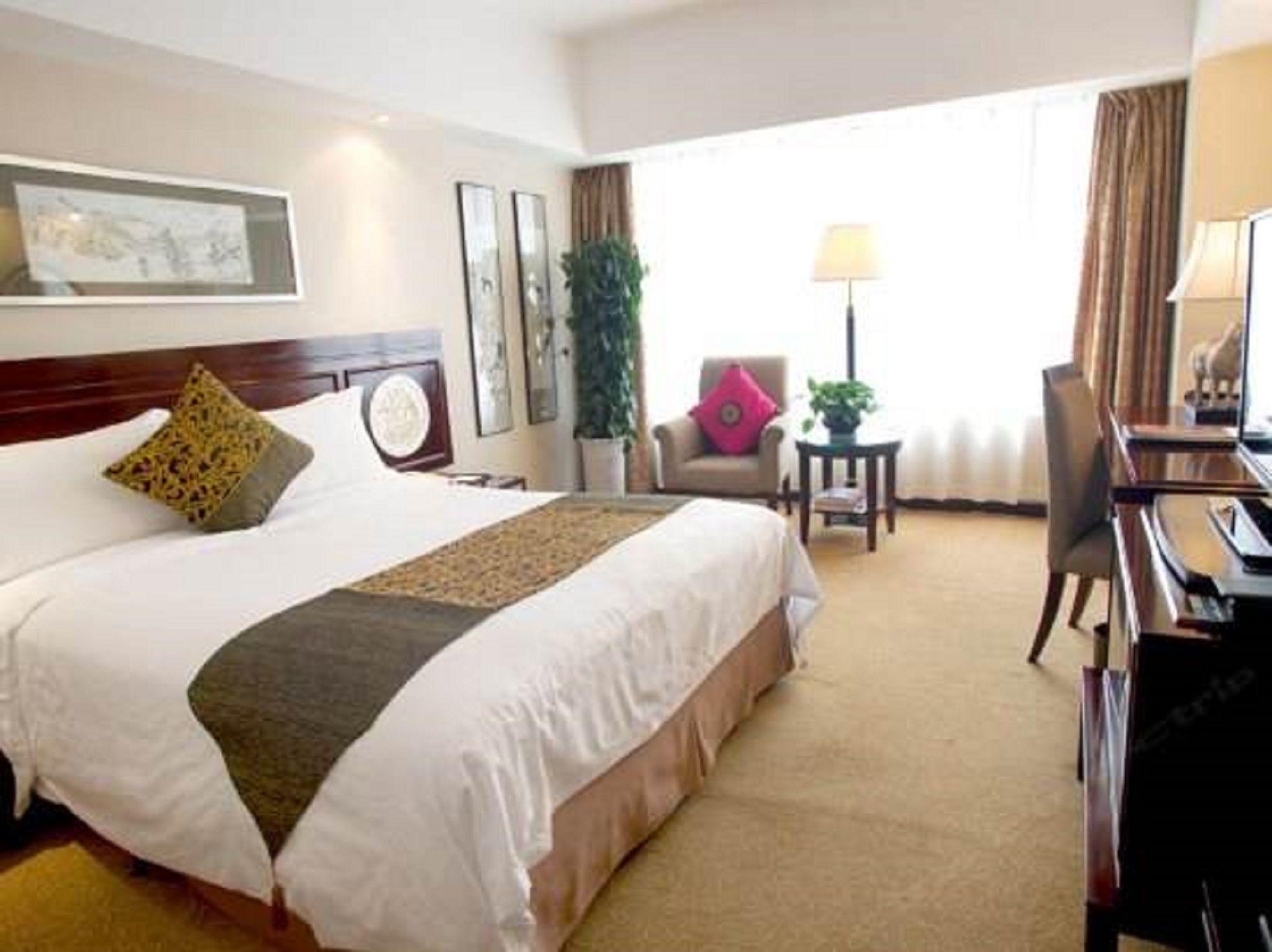 A hotel room with a large bed, a desk, a chair, a lamp, and a window with curtains.