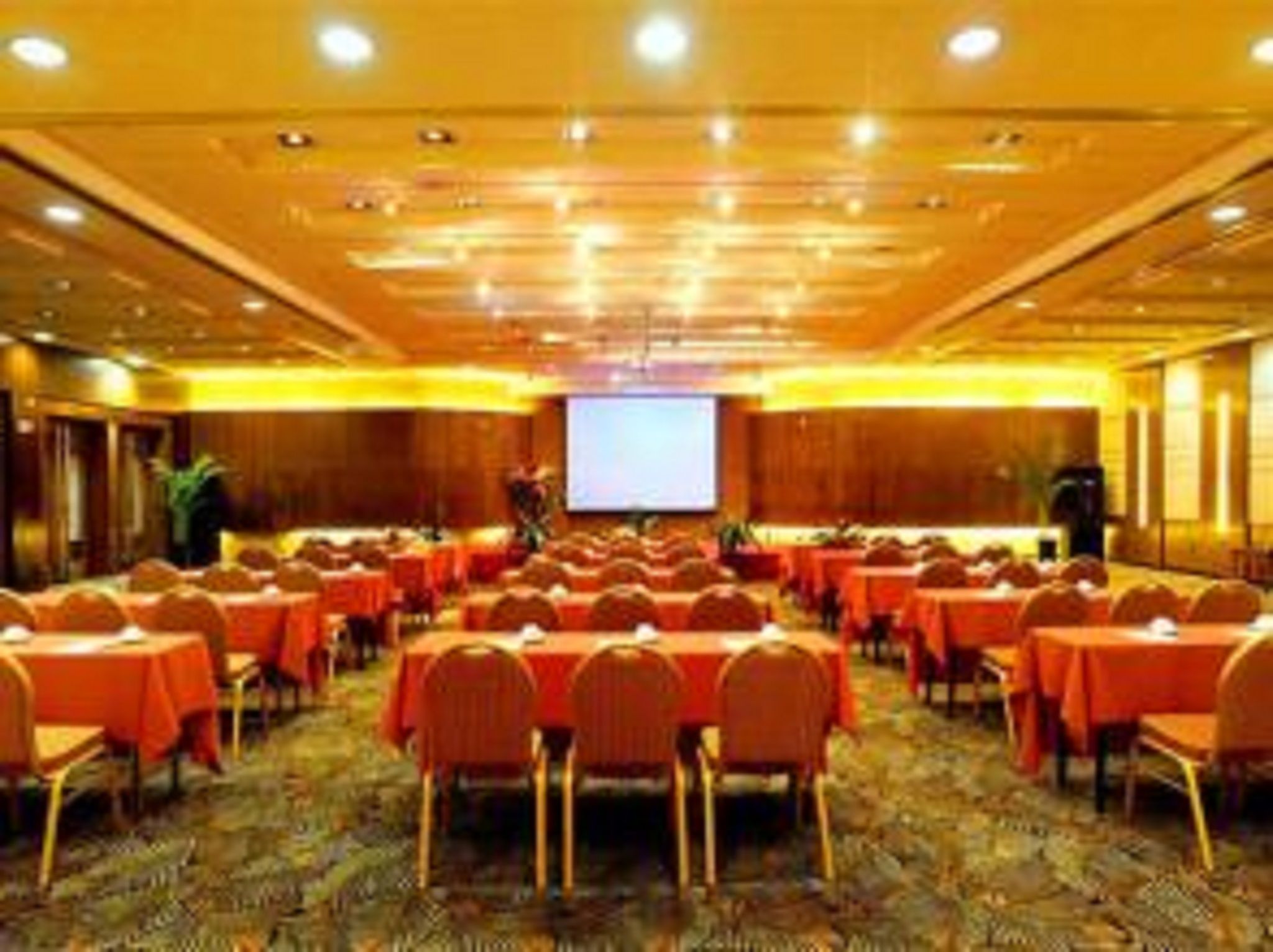 A conference room with rows of tables and chairs, a large screen at the front, and a carpeted floor.