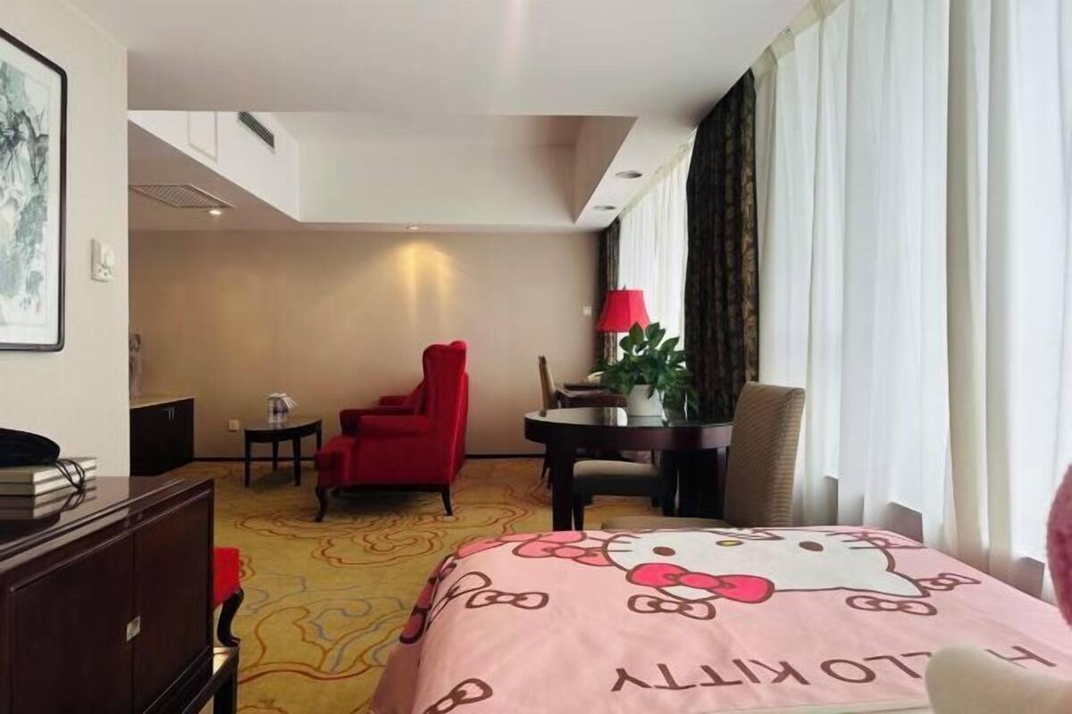 Una habitación de hotel con cama, escritorio, una silla roja, una mesita y una planta en maceta.