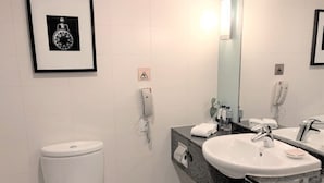 A modern bathroom with a white toilet, a sink with a mirror, and a framed picture on the wall. - Grand Dynasty Culture Hotel (Xi'an)