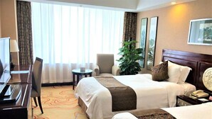 A hotel room with two beds, a desk, a chair, a small table, and a large plant. - Grand Dynasty Culture Hotel (Xi'an)