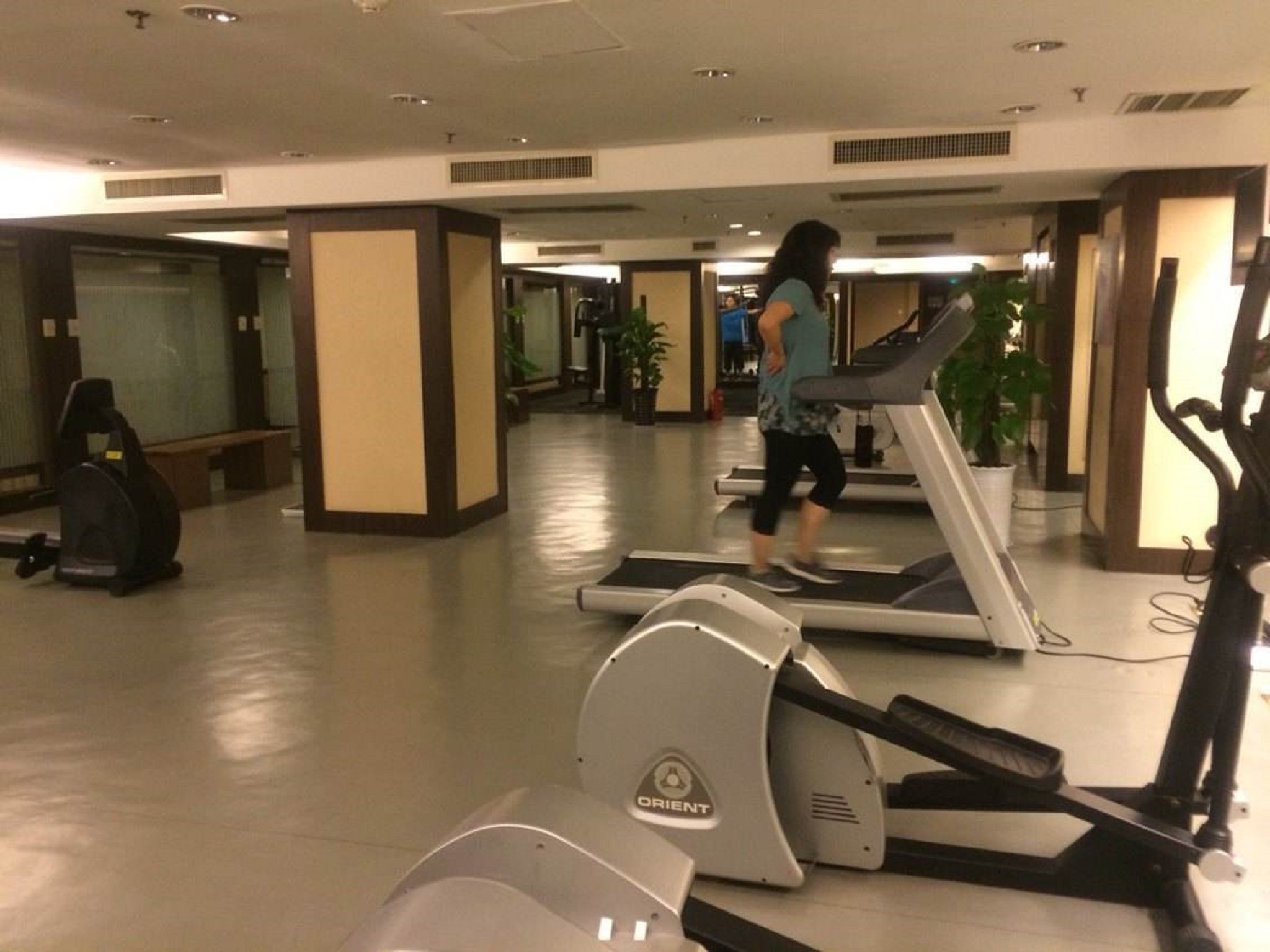 Un gimnasio con cintas de correr, bicicletas estáticas y una persona caminando en una cinta.