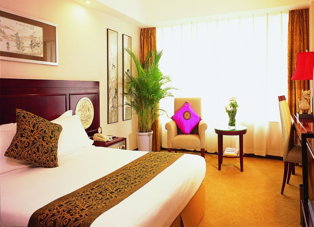 Una habitación de hotel con una cama grande, una silla, una mesita y una planta en maceta.
