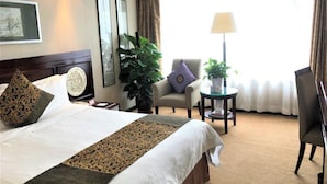 A hotel room with a large bed, a chair, a small table, and a lamp. - Grand Dynasty Culture Hotel (Xi'an)