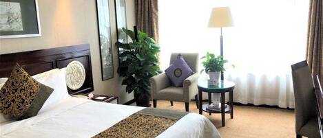 A hotel room with a large bed, a chair, a small table, and a lamp.