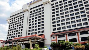 Un hotel grande de varios pisos con un estilo arquitectónico tradicional, que cuenta con una entrada destacada con techo rojo y un letrero en un idioma extranjero.
