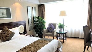 A hotel room with a large bed, two armchairs, a small table, and a window with curtains. - Grand Dynasty Culture Hotel (Xi'an)