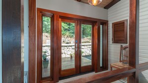 A wooden-framed sliding glass door leading to an outdoor deck with a stone wall and greenery. - Stunning Views, Peaceful Location, Large Pool & Minutes from Cruz Bay (cruz bay)