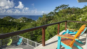 A deck with a pool, two colorful Adirondack chairs, and a view of the ocean and hills. - Stunning Views, Peaceful Location, Large Pool & Minutes from Cruz Bay (cruz bay)