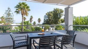 A balcony with a table and chairs, overlooking a garden with palm trees and other greenery.