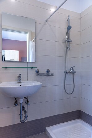 A modern bathroom with a white sink, a glass shelf, a handheld showerhead, and a bathtub.