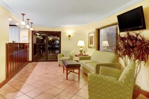 A living room with a sofa, armchair, and a coffee table. There is a TV mounted on the wall and a plant in the corner. - Days Inn at Oak Plantation (Kissimmee)