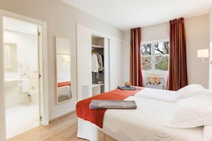 A hotel room with a bed, a wardrobe, a mirror, a window with curtains, and a view of the outdoors.