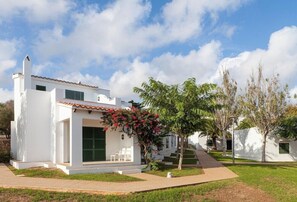 Um edifício moderno branco com telhado de telhas, varanda coberta com cadeiras e um gramado bem cuidado.