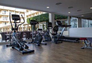 Une salle de sport équipée de machines de cardio, d’un banc et offrant une vue sur un immeuble doté de balcons.