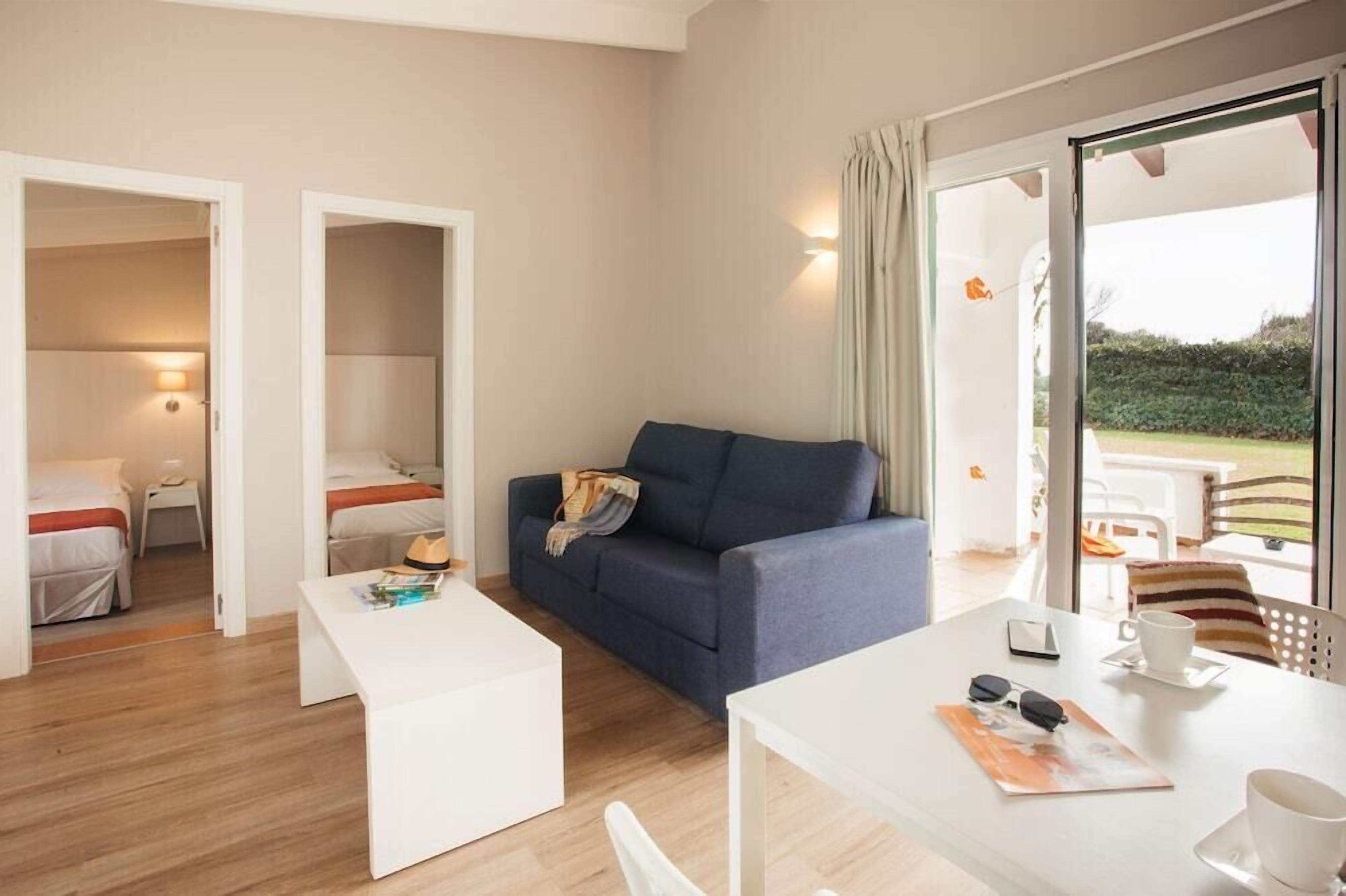 Une chambre d’hôtel moderne avec un canapé, une table à manger et vue sur le jardin.