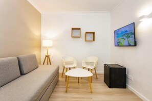 Una sala de estar con un sofá, dos sillones, una mesita, una lámpara de pie, un televisor y un cuadro en la pared.