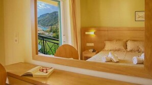 A hotel room with a bed, bedside table, and a window with a view of a mountainous landscape. - Philoxenia Hotel (Corfu)