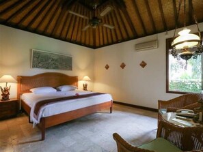 A bedroom with a wooden bed, two bedside lamps, a ceiling fan, and a window with a view of greenery. - Villa Chempaka (Ubud)