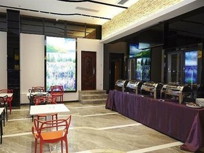 A dining area with tables and chairs, a buffet line, and a large screen displaying a landscape. - Lavande Hotel (Zhanjiang)