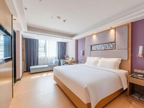 A hotel room with a large bed, a desk, a chair, a window with curtains, and a painting on the wall. - Lavande Hotel (Zhanjiang)