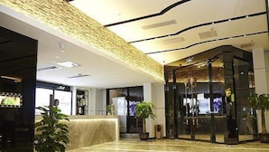 A hotel lobby with a reception desk, a seating area, and a glass elevator. - Lavande Hotel (Zhanjiang)