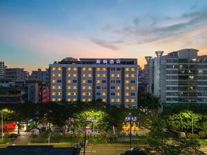 A multi-story hotel with illuminated windows, surrounded by other buildings and trees.