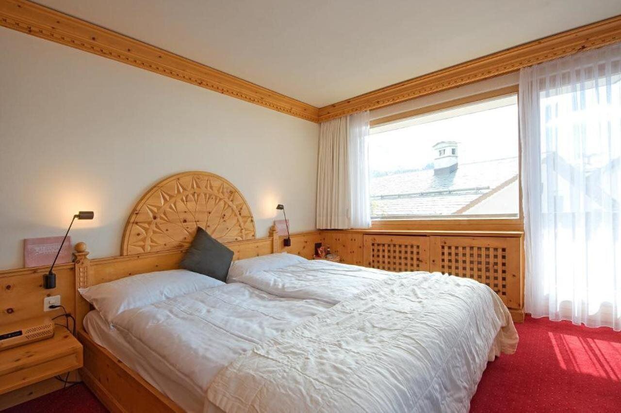 A hotel room with a large bed, wooden headboard, a window with a view of a boat, and a red carpet.