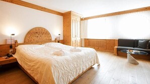 A hotel room with a large bed, a sofa, a small table, and a window with curtains. - Albana (Silvaplana)