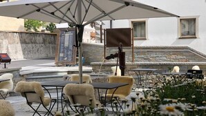 An outdoor seating area with tables and chairs, a large umbrella, and a stone wall in the background. - Albana (Silvaplana)
