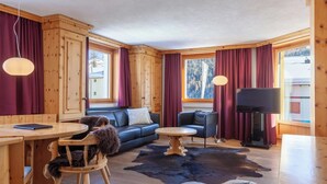 Ein gemütliches Blockhauss-Interieur mit Holzausbau, einer Couch, einem Esstisch, einem Fernseher und großen Fenstern.