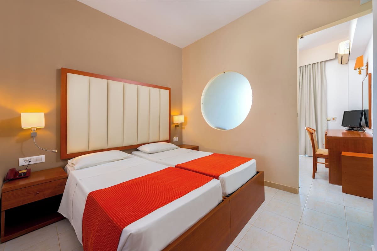 Una camera d'albergo con due letti, una scrivania, una sedia, uno specchio tondo e una lampada.