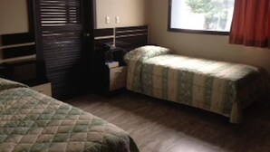 Ein Zimmer mit zwei Betten, einem Nachttisch, einem Fenster mit Vorhängen und einer Tür mit Jalousien.