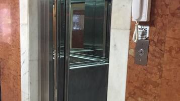 An elevator with a glass door, a wall-mounted intercom, and a tiled floor.