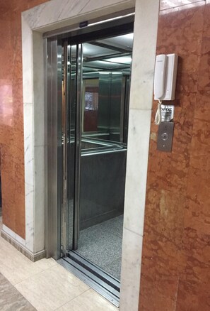 An elevator with a glass door, a wall-mounted intercom, and a tiled floor.