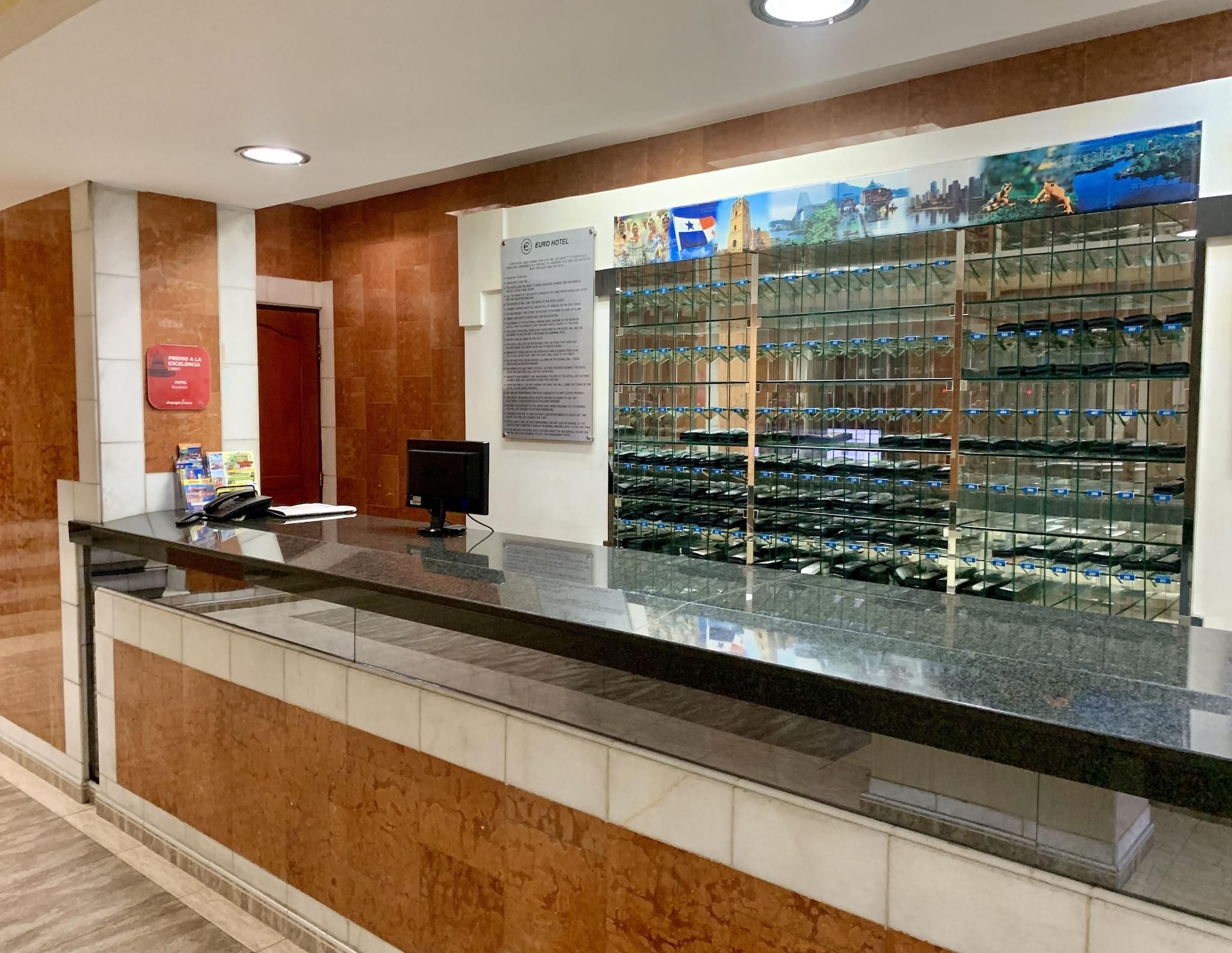 Balcão de recepção de hotel com vitrine de sapatos, uma porta vermelha e um sinal fixado na parede.