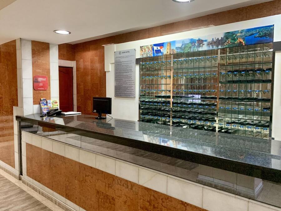 Un mostrador de recepción de hotel con una vitrina de zapatos, una puerta roja y un cartel en la pared.