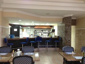 A restaurant with a bar area, multiple tables with chairs, and a kitchen in the background.