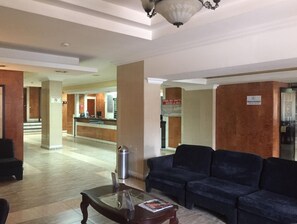 Un hall con mostrador de recepción, un sofá, una mesa de centro y un cubo de basura.