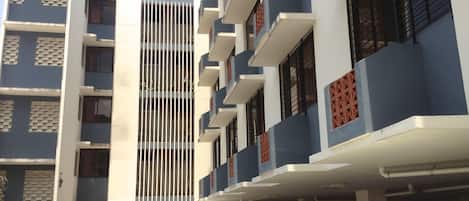 A multi-story building with a central vertical feature, parking spaces, and a clear sky.