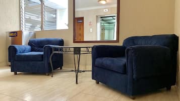 A room with two blue armchairs, a small table, a mirror, and a wooden podium with a sign.