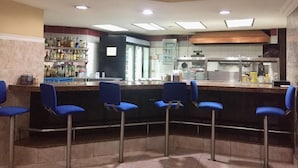 A bar area with four blue bar stools, a counter with a beverage display, and a kitchen in the background. - Eurohotel Panama (Panama City)