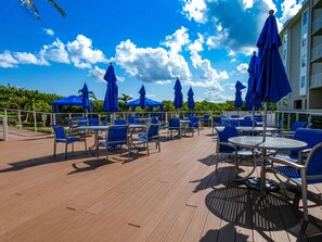 Eine Außenpatio mit blauen Stühlen und Sonnenschirmen, ein Holzdeck und ein Blick auf Himmel und Wolken.