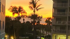Een pad dat naar een gebouw leidt, met uitzicht op palmbomen en een zonsondergang.
