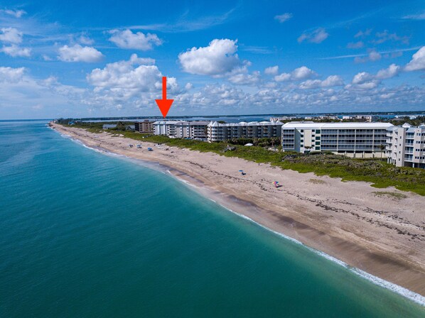 Luftaufnahme eines Küstenhotels mit mehreren Gebäuden, einem Strand und blauem Himmel.