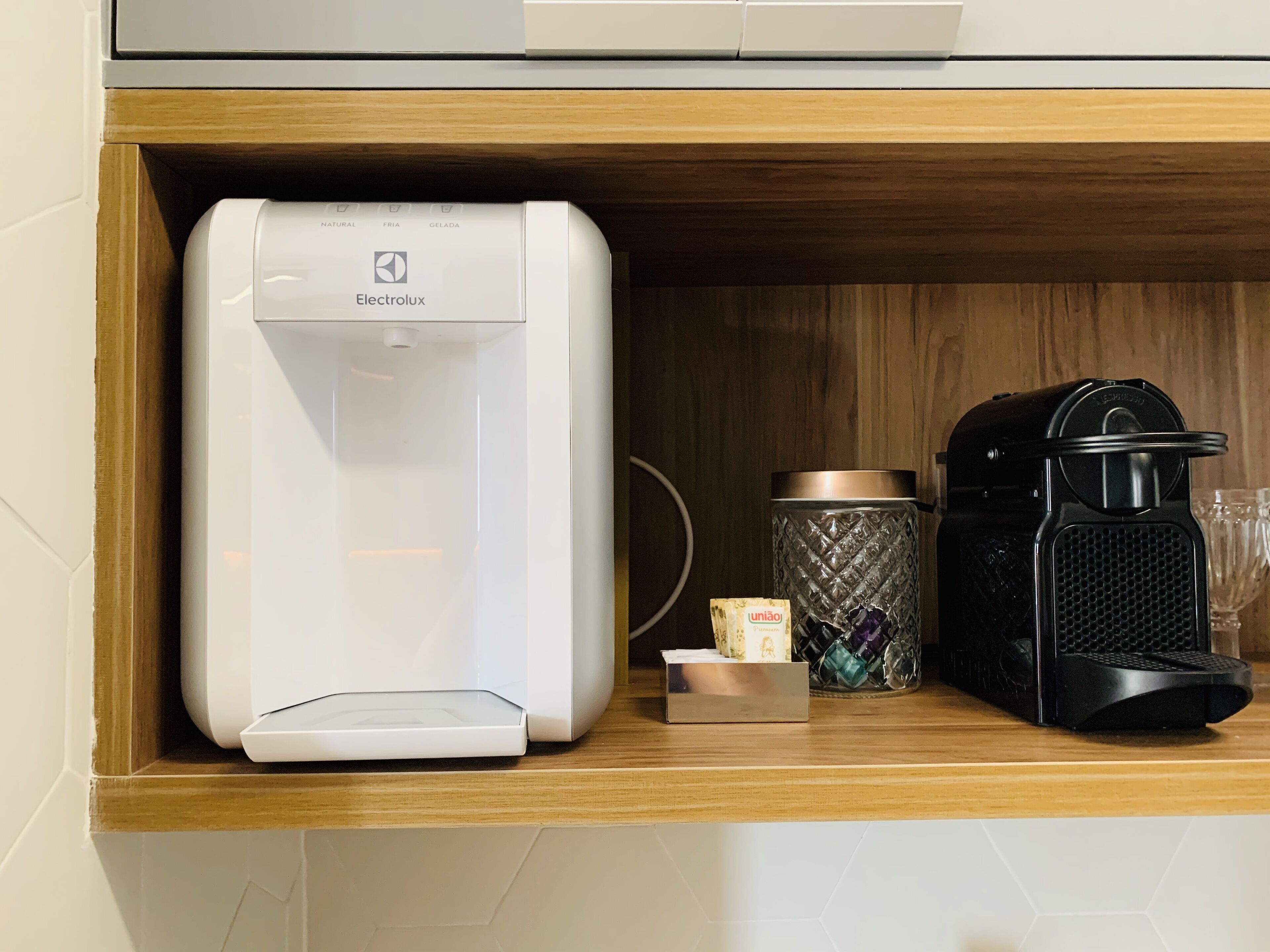 Una zona de cocina con cafetera, dispensador de agua y un recipiente sobre la encimera.