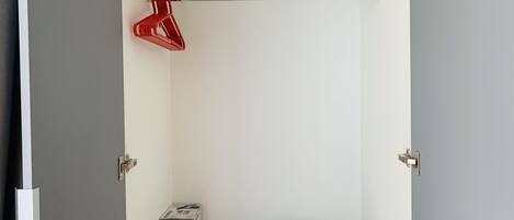 A small, neatly organized closet with a white towel folded on a gray shelf, a red hanger, and a box of a product.