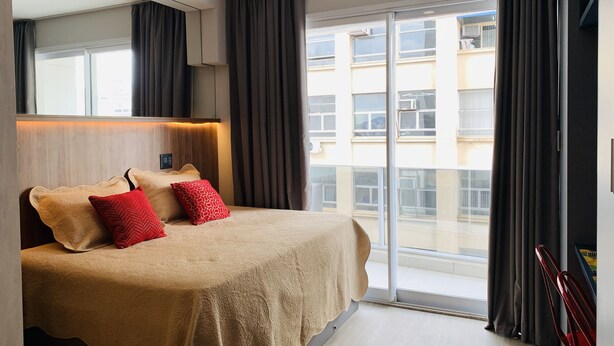 Ein Hotelzimmer mit einem großen Bett, einem Kopfteil mit integrierter Beleuchtung, einer Schiebetür zum Außenbereich und Blick auf die Stadtlandschaft.